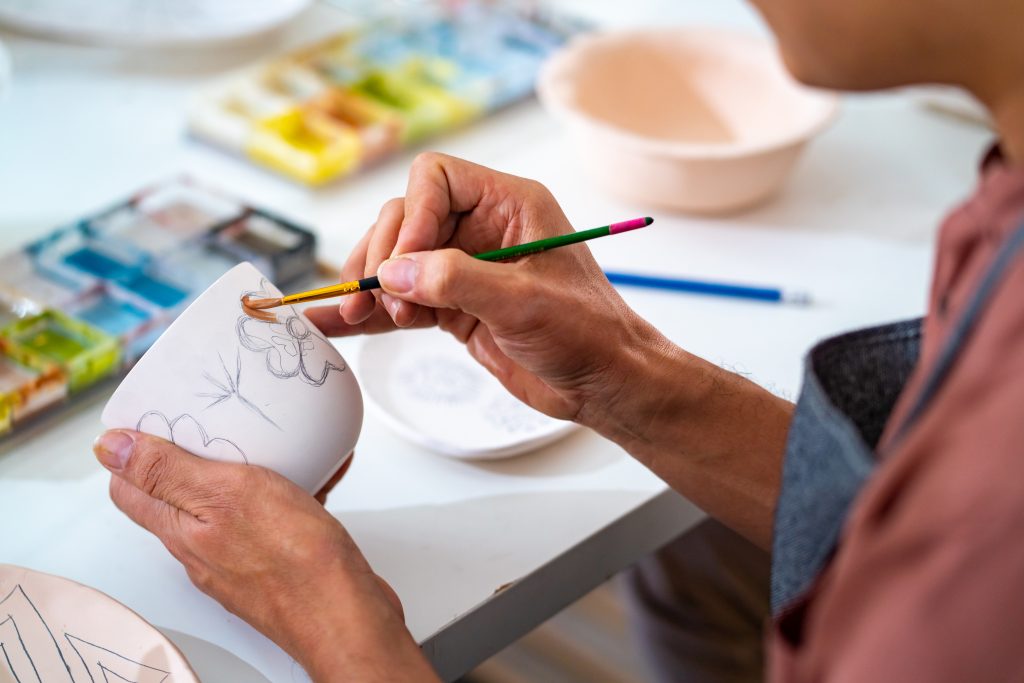 Asian LGBTQ guy learning color painting her self-made pottery at home. Confidence male enjoy hobbies and indoors leisure activity handicraft ceramic sculpture and painting workshop at pottery studio