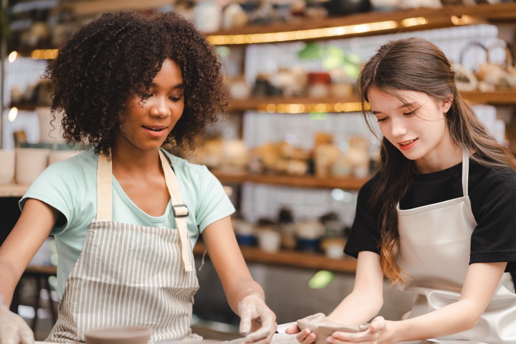 Two multi-ethnic friend is enjoy a having fun while learning a pottery or sculpture workshop, school's pottery clay class students, therapy hobbies, creativity and ideas, handcraft free time activity.